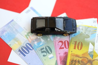 İsviçre frangı banknotları ve bayrak üstünde oyuncak araba. Mevcut frank, faturalar ve siyah araba bayrağın üzerinde duruyor. İsviçre 'de araba sahibi olma kavramı