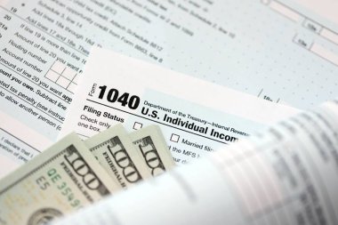 Yüz dolarlık banknotlar ve 1040 bireysel gelir vergisi iade formu yakın çekim. Çok az Amerikan doları ve Birleşik Devletler vergisi yok. ABD 'de vergi ödeme ve muhasebe kavramı