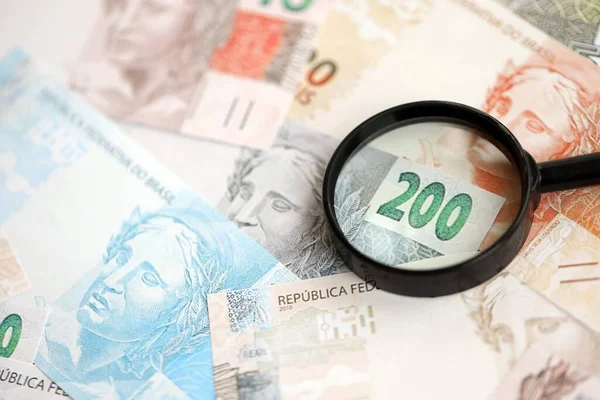 Brezilya reais banknotları ve büyüteç. Mevcut Brezilya gerçek para faturaları ve loupe büyük miktarda masada yatıyor. Brezilya 'da mali izleme ve vergilendirme kavramı
