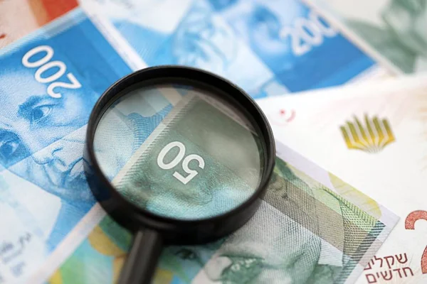 Israel New Shekels banknotları ve büyüteç. Şu anki İsrail 'in yüksek meblağlı faturaları masanın üzerinde yatıyor. İsrail 'de mali izleme ve vergilendirme kavramı