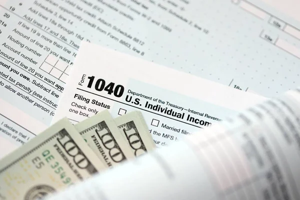 Yüz dolarlık banknotlar ve 1040 bireysel gelir vergisi iade formu yakın çekim. Çok az Amerikan doları ve Birleşik Devletler vergisi yok. ABD 'de vergi ödeme ve muhasebe kavramı