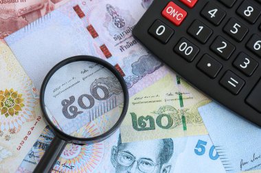 Tayland baht para birimi faturaları ve yakınlaştırıcı bardaklı hesap makinesi. Vergilendirme ve para sayımı kavramı