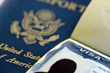 Açık pasaport sayfasında ABD vizesi ve arka planda ABD pasaport kapağı