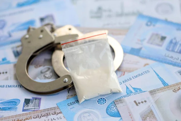 Birleşik Arap Emirlikleri kara para birimi faturaları ve kelepçeli kokain paketleri. Uyuşturucu suçları kavramı