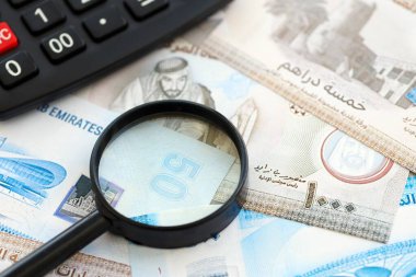 Birleşik Arap Emirlikleri kara para birimi faturaları ve büyüteçle yakınlaştırılmış hesap makinesi. Vergilendirme ve para sayımı kavramı