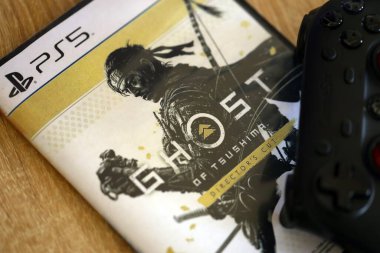 KYIV, UKRAINE - SEPTEMBER 8, 2025 Ghost of Tsushima videogame lies on brown wooden table with black gamepad close up