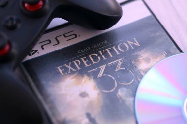 KYIV, UKRAINE - SEPTEMBER 8, 2025 Clair Obscur Expedition 33 videogame lies on wooden table with disc and black gamepad close up