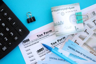 Birleşik Arap Emirlikleri kara para faturaları ve mavi üzerine yakın vergi formlu hesap makinesi. Vergi ve muhasebe kavramı