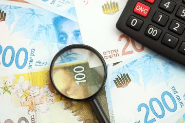 Israel New Shekels banknotları ve büyüteçle birlikte hesap makinesi. Mevcut İsrail para faturaları ve loupe ile calc büyük miktarda masada yatıyor. İsrail 'de vergilendirme ve para kavramı