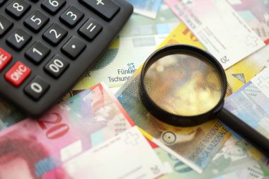 İsviçre frangı banknotları ve büyüteçli hesap makinesi. Mevcut para faturaları ve loupe ile calc büyük miktarda masada yatıyor. İsviçre 'de vergilendirme ve iş kavramı