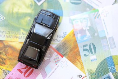 İsviçre frangı banknotları ve oyuncak araba. Mevcut frank, faturalar ve siyah araba büyük miktarda masada yatıyor. İsviçre 'de araba sahibi olma kavramı