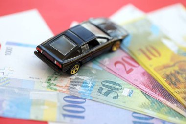 İsviçre frangı banknotları ve bayrak üstünde oyuncak araba. Mevcut frank, faturalar ve siyah araba bayrağın üzerinde duruyor. İsviçre 'de araba sahibi olma kavramı