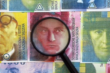 İsviçre frangı banknotları ve büyüteç. Loupe 'un para faturaları büyük miktarda masada duruyor. İsviçre 'de mali izleme ve vergilendirme kavramı