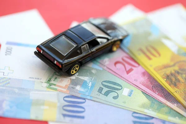 İsviçre frangı banknotları ve bayrak üstünde oyuncak araba. Mevcut frank, faturalar ve siyah araba bayrağın üzerinde duruyor. İsviçre 'de araba sahibi olma kavramı