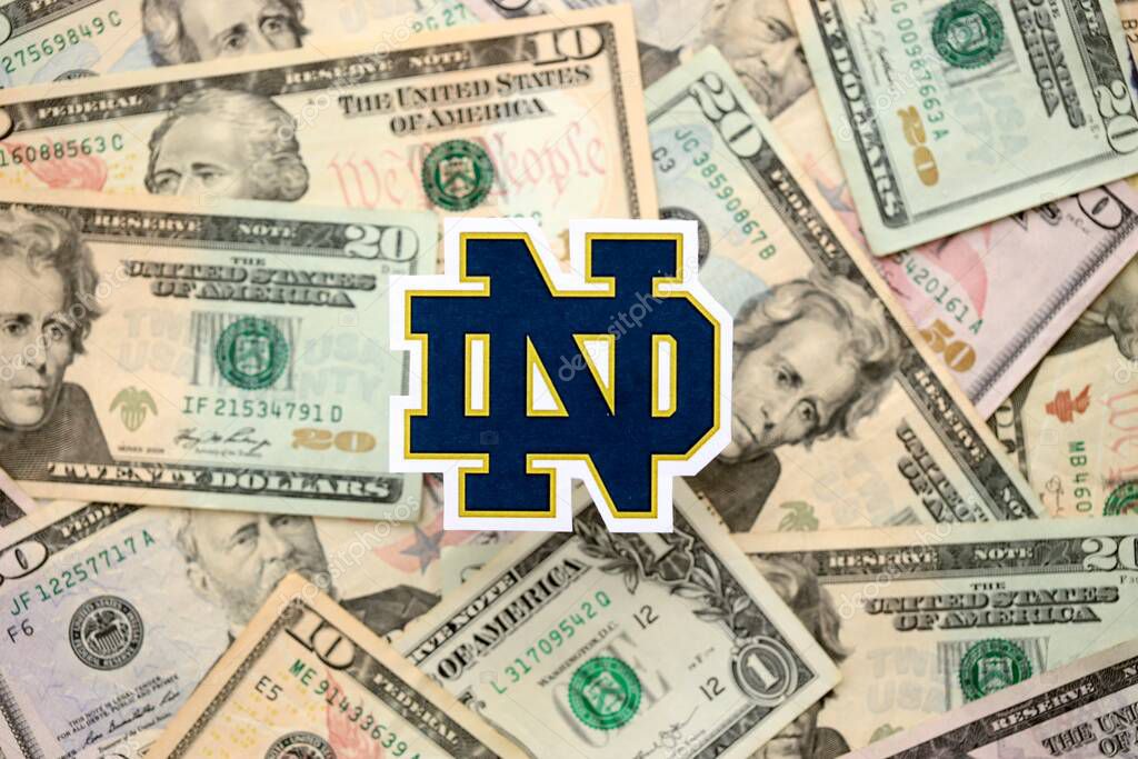KYIV, UKRAINE - FEBRUARY 23, 2025 Notre Dame Fighting Irish basketball team badge lies on big amount of US dollar bills close up