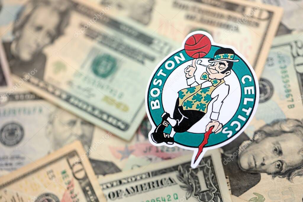 KYIV, UKRAINE - FEBRUARY 23, 2025 Boston Celtics basketball team badge lies on big amount of US dollar bills close up