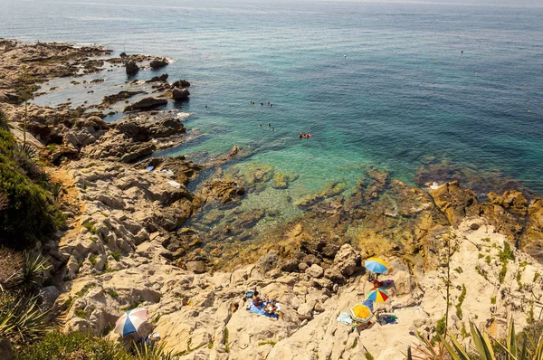 在意大利里维埃拉的岩石海滩清澈的水与彩色沙滩遮阳伞在夏天 — 图库照片
