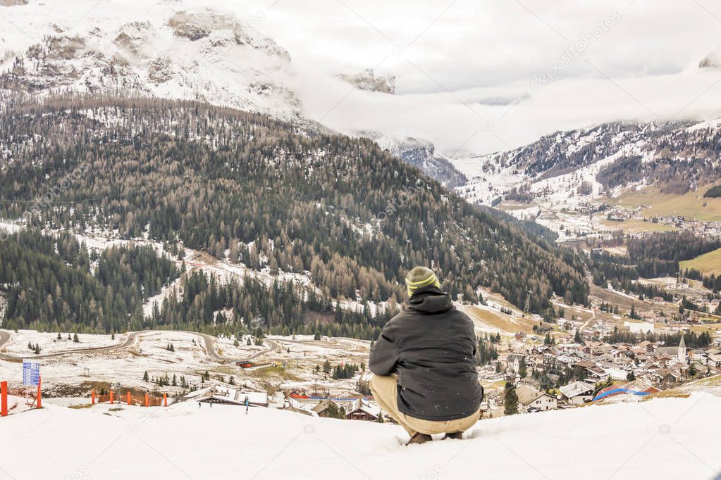 Young man sitting on the snow and watching the Alta Badia valley near Corvara
