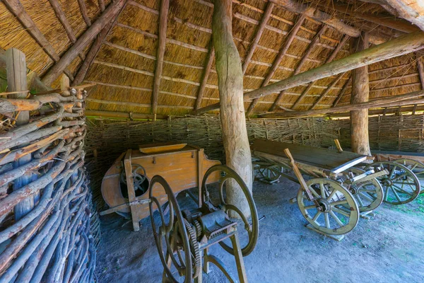 Alat kuno untuk memotong rumput, gerobak dengan roda kayu dan lingkaran besi di atasnya. Berdiri di gudang dengan atap jerami — Stok Foto