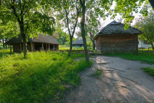 A wooden house with a thatched roof and a cowshed with beams and branches. Simple and practical — Stock Photo, Image