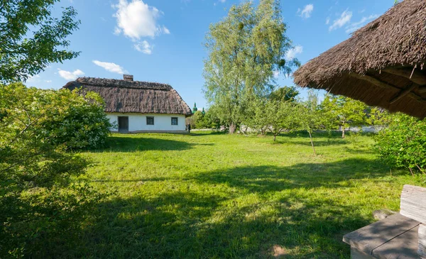 Uma casa velha com telhado de palha em um gramado verde no parque — Fotografia de Stock
