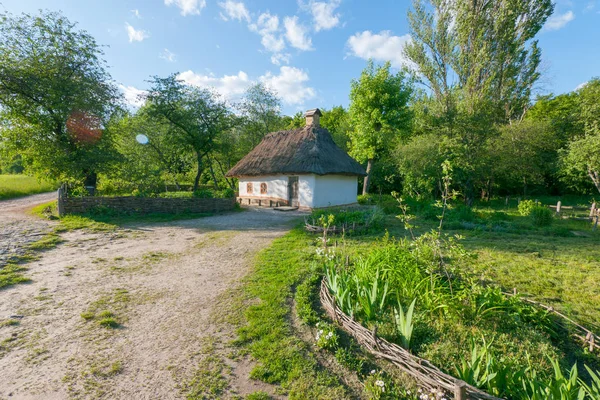 Velha casa ucraniana de uma cabana de lama em uma aldeia em um gramado verde em um céu nublado azul — Fotografia de Stock