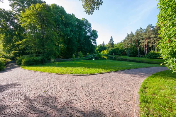 El camino está trazado con un pavimento de piedra en un hermoso parque verde en un día nublado de verano. Un buen lugar para relajarse junto al lago . — Foto de Stock
