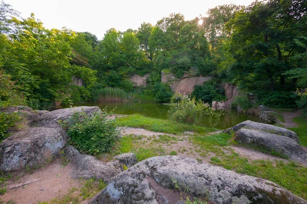 A small green transparent lake on a background near stone boulders and green vegetation