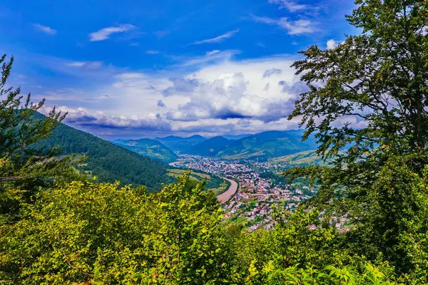 Magnífico paisaje del valle de la montaña con la ciudad acostada. Con picos de color verde esmeralda y densas nubes blancas sobre ellos . — Foto de Stock