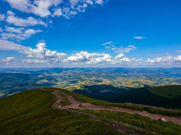 Estrada de terra no cume de uma montanha alta coberta com grama densa verde subindo para um céu azul com nuvens — Fotografia de Stock