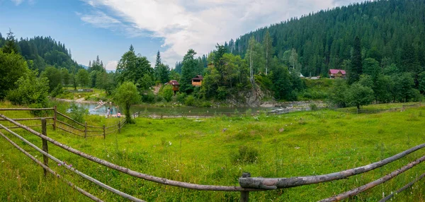 Beautiful views of the mountainous terrain with the current river between the low banks with green grass on one side and trees and houses on the other. — Stock Photo, Image