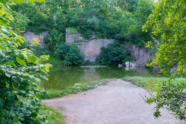 Ein kleiner Teich mit Schmutzwasser und ein verstopfter Stapel zwischen den grünen Bäumen — Stockfoto