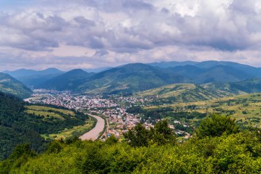 Yeşil ormanlar ve yüksek dağlarla çevrili bir nehir kıyısında güzel bir kasaba