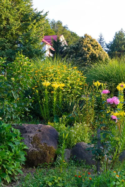 一花坛, 周围有大鹅卵石和花。它是可见的金盏花, 粉红色的玫瑰和其他一些黄色的花朵 — 图库照片