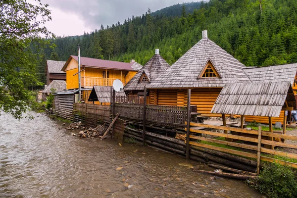 Wooden Hutsul manor on the steep bank of the river at the foot of the mountains in the Carpathians — Stock Photo, Image