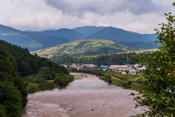 Góry krajobraz, panorama górskiej rzece, wieś, zielone łąki i stoki na tle pochmurnego nieba — Zdjęcie stockowe