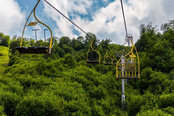 Téléphérique avec cabines pour trois sièges et balustrades jaunes sur fond d'arbres verts luxuriants — Photo