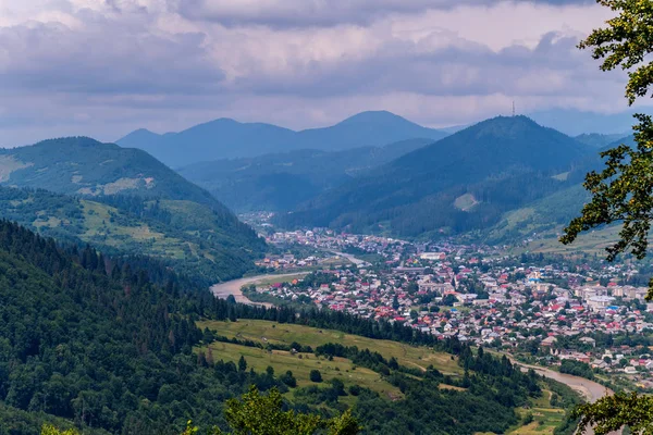 Las cimas azules de las montañas en la niebla, el cielo inquieto en las nubes y una pequeña ciudad con casas de un solo piso de color — Foto de Stock