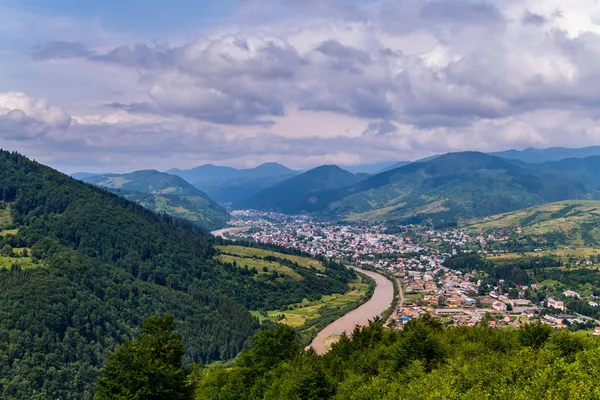 Schlange geschwungener Fluss fließt aus den Wäldern rund um die Stadt und verschwindet dann irgendwie in den Bergen — Stockfoto