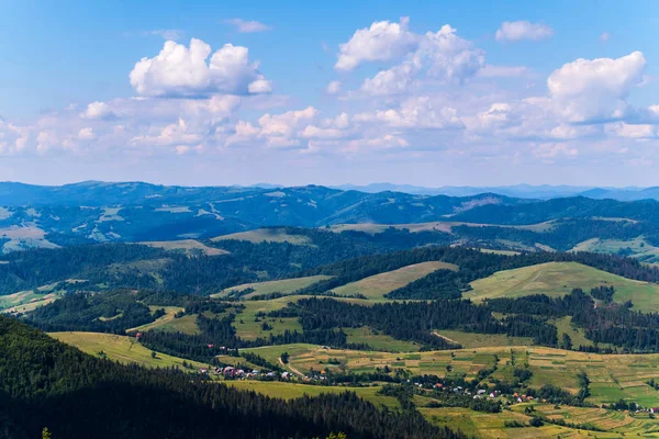 Pueblo en un valle de montaña, árboles verdes y cielo azul con nubes — Foto de Stock