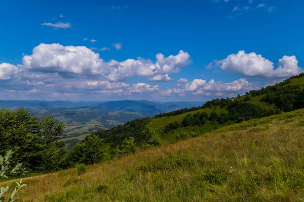 Grasbewachsene abfallende Abfahrt, mit Blick auf die Landschaft der Berge und Hügel unter blauem Himmel — Stockfoto