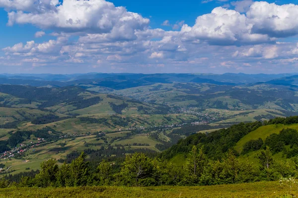 Panorama con cordilleras verdes y pequeñas casas en un valle bajo un cielo nublado — Foto de Stock