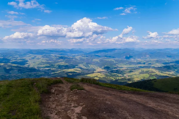 Uma estrada de uma montanha que conduz a um vale entre as colinas cobertas de verdes em um dia nublado — Fotografia de Stock