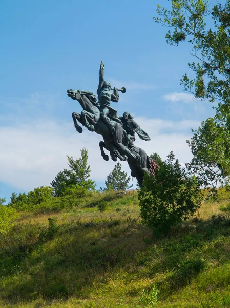 木および青い曇り空の下で薮の中で緑の丘の馬のギャロッピングの記念碑 — ストック写真