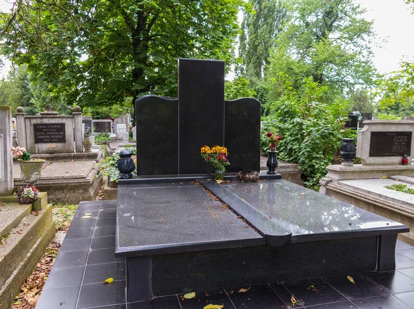 Large black marble slab gravestone in the cemetery with a standing bouquet of flowers with fallen leaves. — Stock Photo, Image