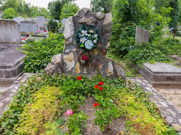 Tombstone on the grave carved from a large stone with flowers attached to it and planted next to the green shoots. — Stock Photo, Image