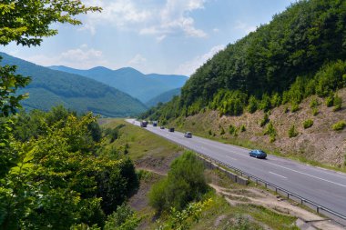 mavi bir gökyüzü ve mesafe Peaks'e karşı ormanlık tepeler arasında bir dağ yolu boyunca sürüş araba