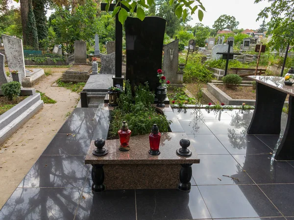 Un monumento de granito negro con dos lámparas rojas en primer plano y una cruz —  Fotos de Stock