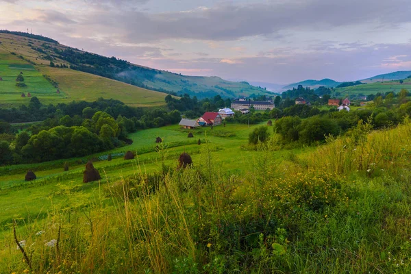 Großer grüner Balken. Am nächsten Hang liegen mehrere Heuhaufen mit braunem Heu, das offenbar vom Regen durchnässt wurde. — Stockfoto