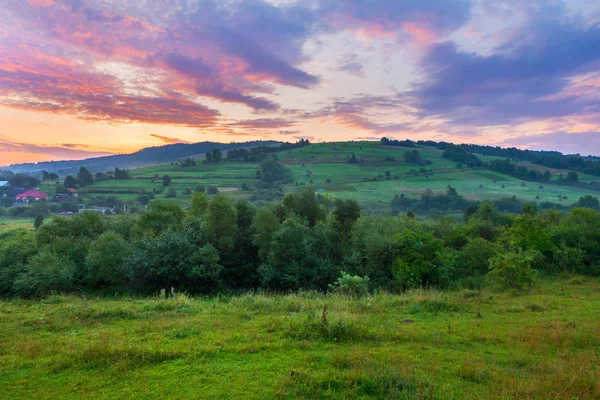 Grön bergssluttning med hus på det mot bakgrund av en gryning eller solnedgång sky. plats för vila och resa — Stockfoto